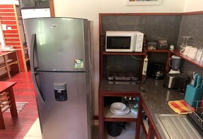 Una kitchenette compacta con un refrigerador de acero inoxidable, un microondas, una cafetera y una estufa a gas.