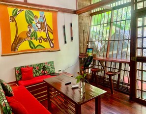 Une pièce avec une table en bois, un canapé rouge et une grande fenêtre donnant sur un paysage verdoyant.