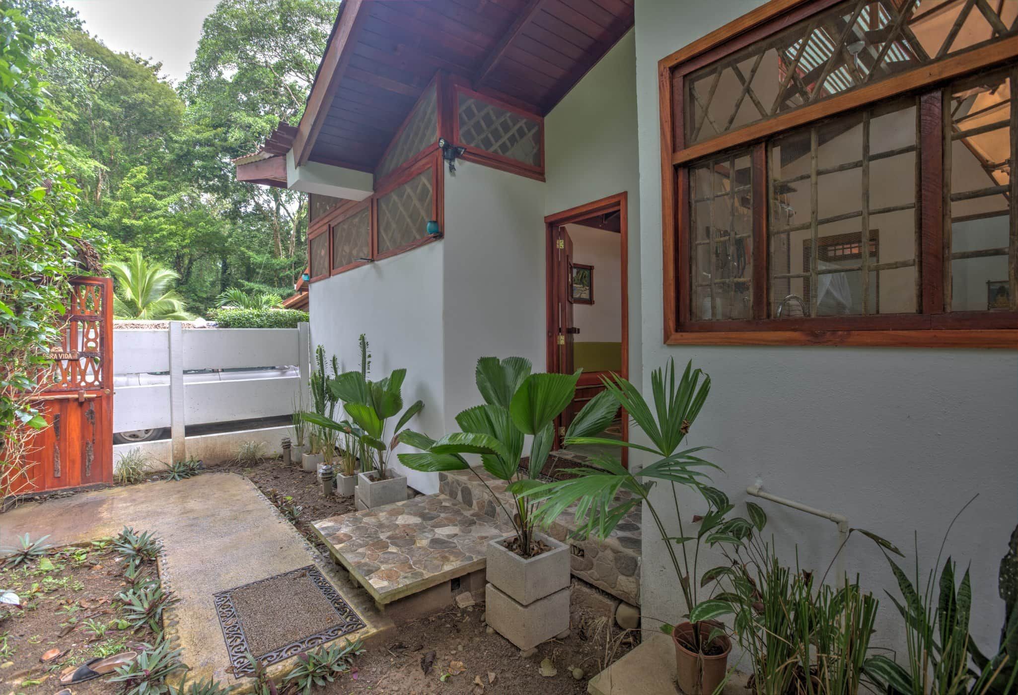 Une maison avec un chemin de pierre menant à l’entrée, entourée de plantes en pot et d’un petit jardin.