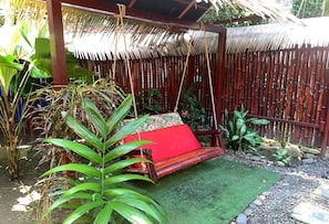 A hammock chair with a red cushion, surrounded by lush greenery and a bamboo fence.