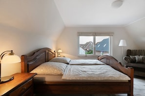 Une chambre à coucher avec un lit en bois, des lampes de chevet, une fenêtre donnant sur des maisons et un canapé.