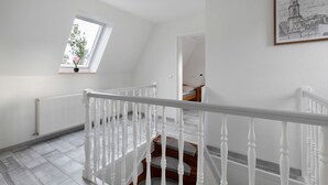 Eine Treppe mit weißen Balustraden, ein Heizkörper, ein Fenster mit Pflanze und ein gerahmtes Bild an der Wand.