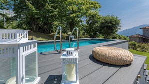 A poolside area with a clear view of a swimming pool, a wooden deck, and a wicker ottoman. - Casa Bandoni, Bagni di Lucca, Lucca and Viareggio (Bagni di Lucca)
