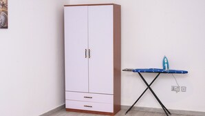 A white wardrobe with two doors and a small drawer, next to a blue ironing board with an iron. -  1-bedroom apartment with WiFi, fitness room in amazing Accra (Accra)