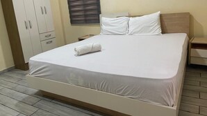 A neatly made bed with a white sheet and a rolled towel, a wooden wardrobe, and a window with blinds. -  1-bedroom apartment with WiFi, fitness room in amazing Accra (Accra)