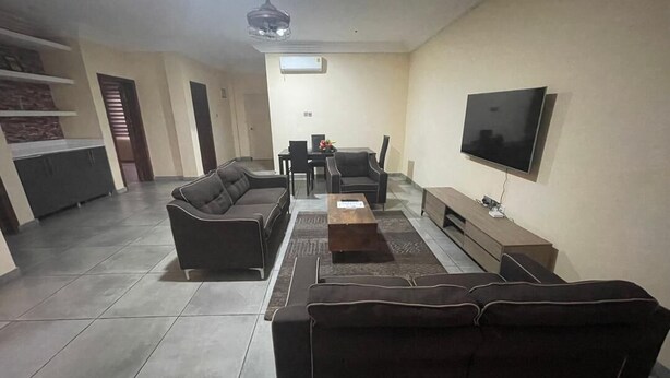 A living room with a sofa, TV, and a dining area with chairs and a table. -  1-bedroom apartment with WiFi, fitness room in amazing Accra (Accra)