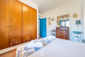A bedroom with a large wardrobe, a bed with a floral bedspread, a dresser, a mirror, and a small table.