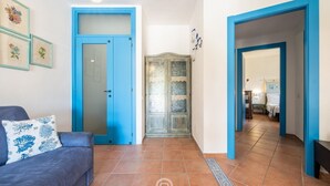 A living room with a blue door, a sofa with a blue cushion, and a hallway leading to a bedroom. - Villa Aurora - Villasimius Paradise (Villasimius)