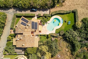 An aerial view of a property with a swimming pool, solar panels, and a well-maintained garden.
