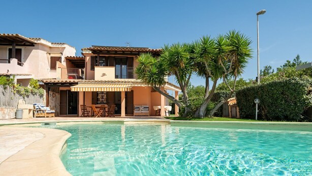 A poolside view of a Mediterranean-style villa with a two-story structure, outdoor seating, and a well-maintained lawn. - Villa Aurora - Villasimius Paradise (Villasimius)