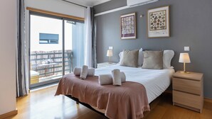 Une chambre moderne avec un grand lit, deux tables de chevet, une fenêtre donnant sur un beau paysage et un climatiseur fixé au mur.