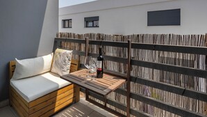 Un balcon avec un canapé en bois, une table avec des verres à vin et une bouteille, et une clôture en bambou.