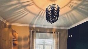 Une chambre avec deux lits, un bureau et une chaise. Il y a une fenêtre avec des rideaux et un luminaire suspendu.