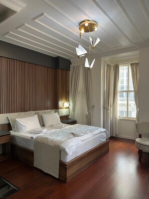 A bedroom with a wooden bed, a nightstand, a bedside lamp, a window with curtains, and a ceiling light fixture. - Şah Bey Konağı (Istanbul)