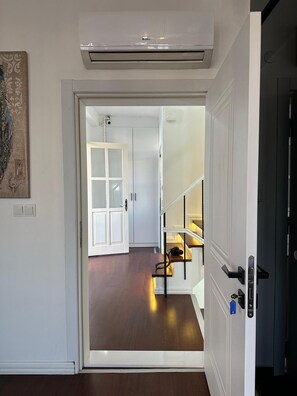 An interior hallway with a wooden floor, a white door leading to a room with a white door, and a staircase with a black railing. - Şah Bey Konağı (Istanbul)