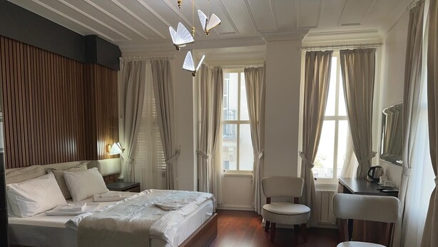 A hotel room with a bed, bedside table, chair, desk, and a view of the outside. - Şah Bey Konağı (Istanbul)