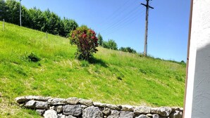 A patio with two black mesh chairs, a stone wall, and a grassy hill with a bush in the background. - Vacation apartment zum Hochgrat (Oberstaufen)