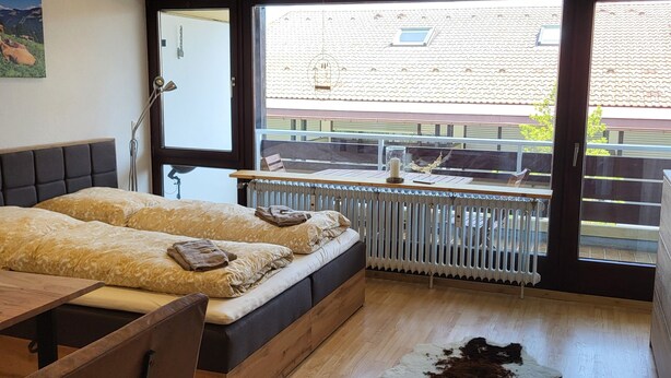 A modern bedroom with a large window, a bed, a wooden desk, and a cowhide rug. - Vacation apartment zum Hochgrat (Oberstaufen)