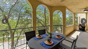 Une terrasse extérieure avec une table ronde prévue pour quatre personnes, entourée de chaises, et un barbecue à l’arrière-plan.