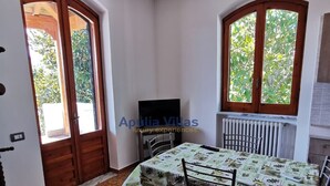 Zona pranzo con tavolo, sedie, lampadario e finestra vista su spazi verdi.