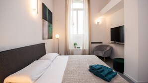Una habitación de hotel moderna con una cama grande, un televisor de pantalla plana, una silla y una ventana con cortinas.