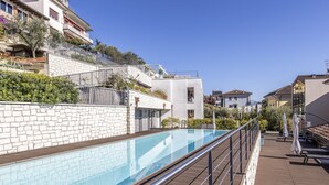 Una piscina con plataforma de madera y barandillas de metal, rodeada de muros de piedra y edificios residenciales.