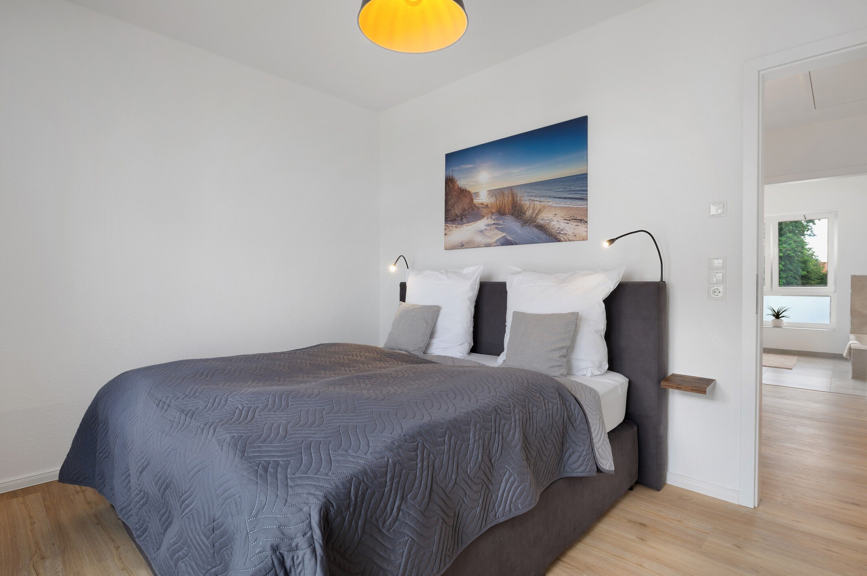 A modern bedroom with a bed, a painting of a beach, and a bedside table.