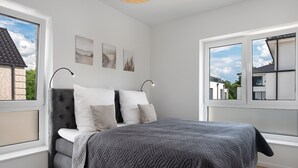 A modern bedroom with a large bed, a window with a view of buildings, and artwork on the wall. - Holiday Home 'Das Strandhaus' with Private Terrace, Private Garden and Wi-Fi (Lembruch)