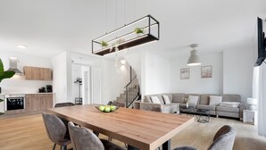 A modern kitchen with wooden cabinets, a dining table with chairs, a staircase, and a living area with a sofa and a TV. - Holiday Home 'Das Strandhaus' with Private Terrace, Private Garden and Wi-Fi (Lembruch)