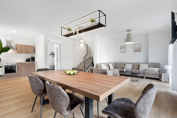 Eine moderne Küche mit Holzausbau, einem Esstisch mit Stühlen, einer Treppe und einem Wohnbereich mit Sofa und Fernseher.