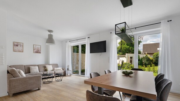 A modern living room with a sofa, coffee table, and dining table. - Holiday Home 'Das Strandhaus' with Private Terrace, Private Garden and Wi-Fi (Lembruch)