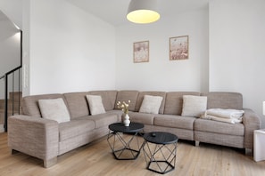 Ein modernes Wohnzimmer mit einem Ecksofa, zwei runden Tischen und einer Pendelleuchte.
