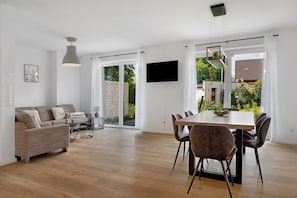 Ein modernes Wohnzimmer mit einer Couch, einem Esstisch, Stühlen, einem Fernseher und einem großen Fenster.
