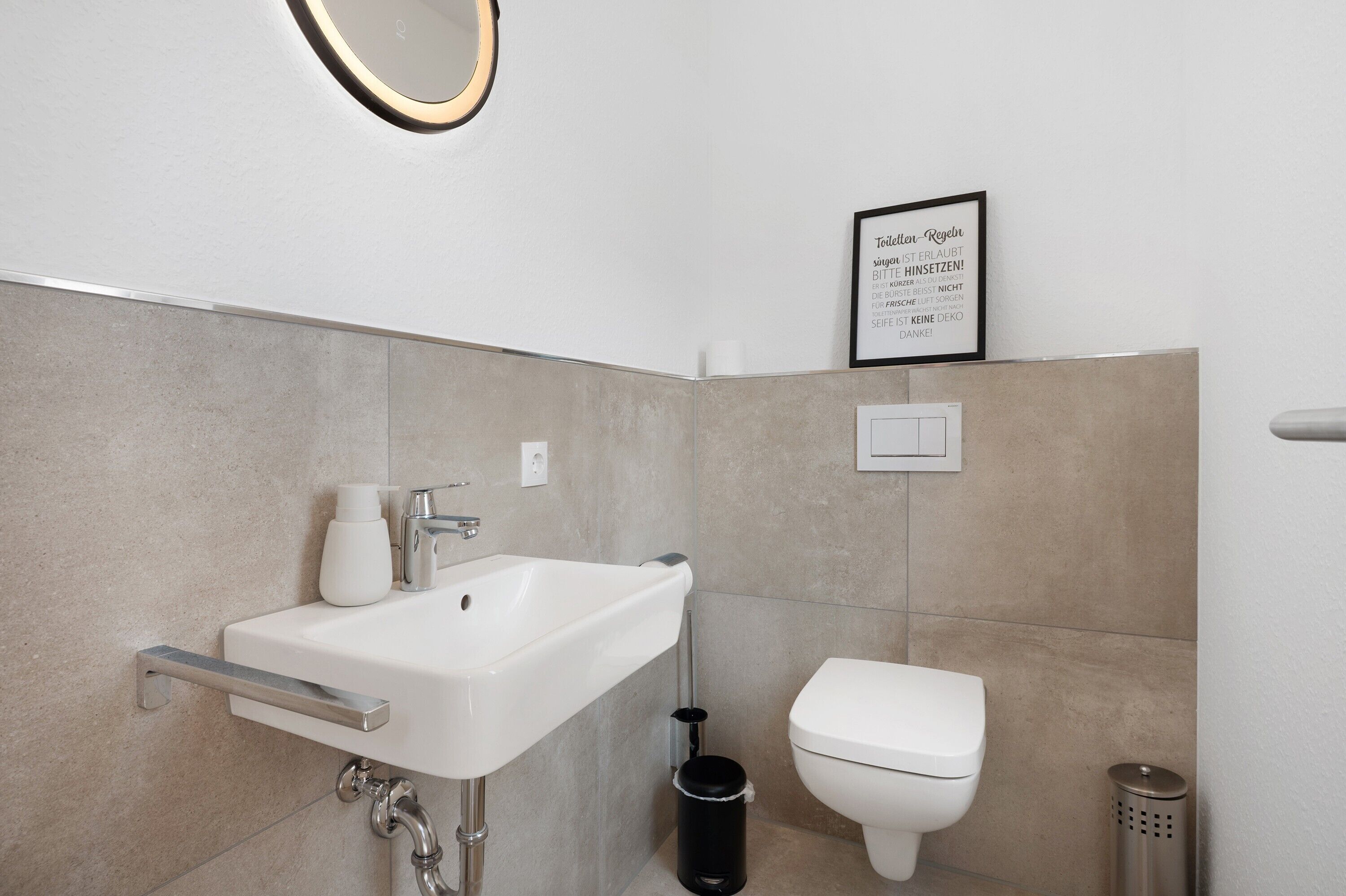A modern bathroom with a white sink, toilet, and trash can.