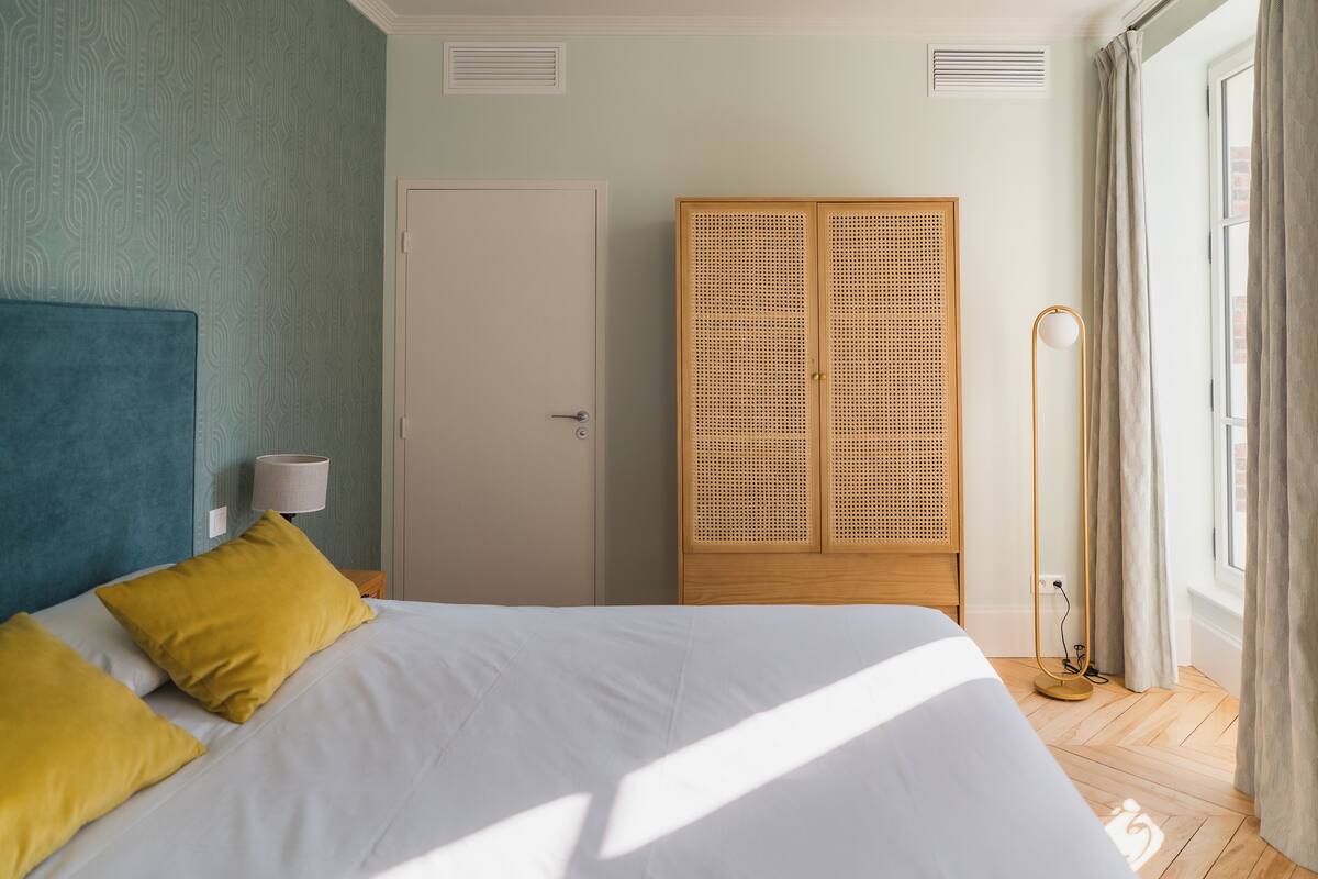 A bedroom with a bed, two pillows, a wardrobe, a floor lamp, and a window with curtains.