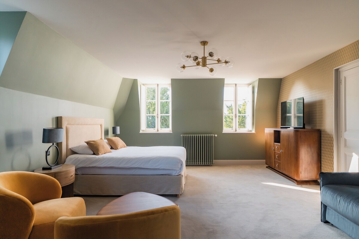 A bedroom with a bed, a nightstand, a lamp, a dresser, a television, and a window.