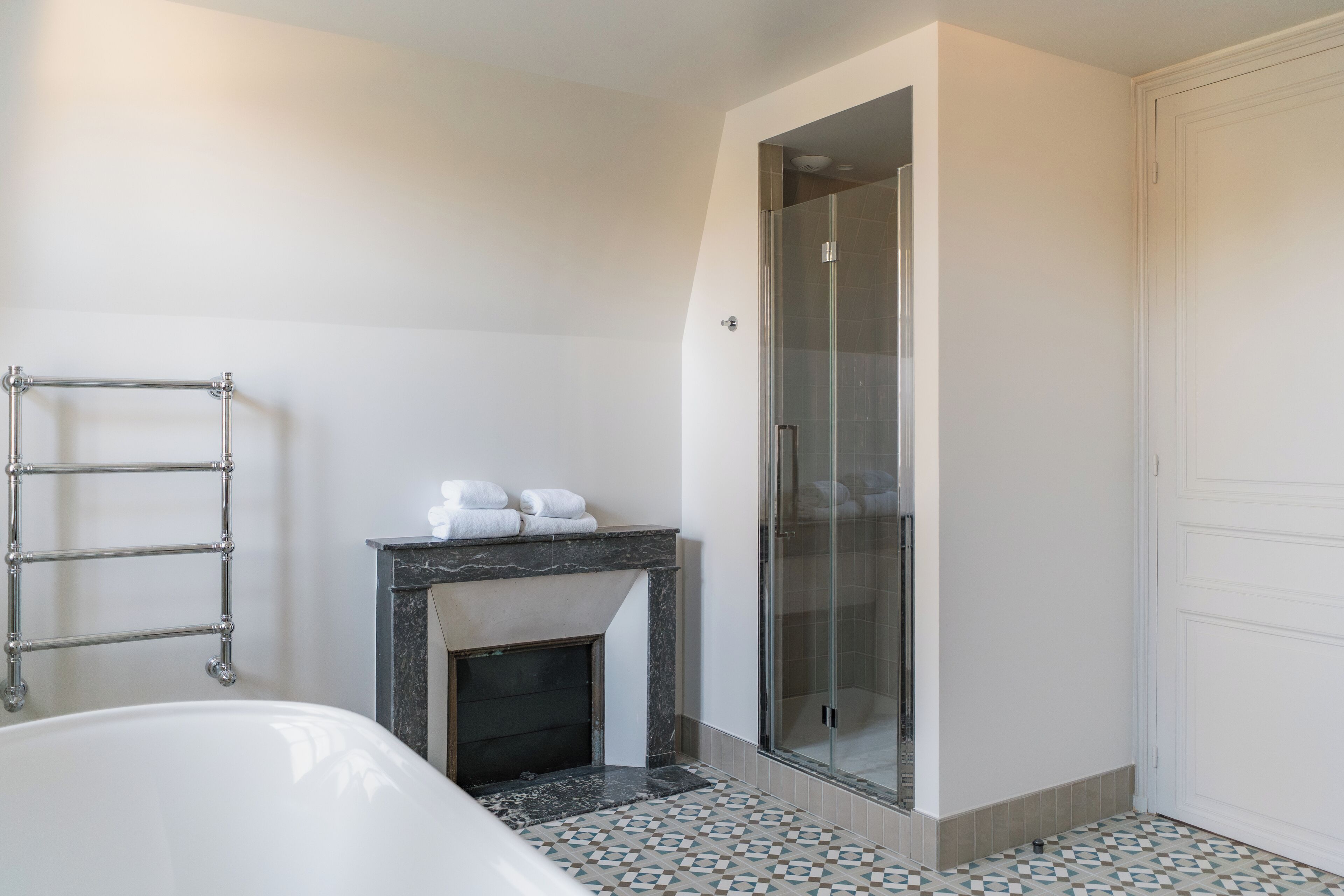 A modern bathroom with a bathtub, a glass-enclosed shower, a marble fireplace, and a tiled floor.