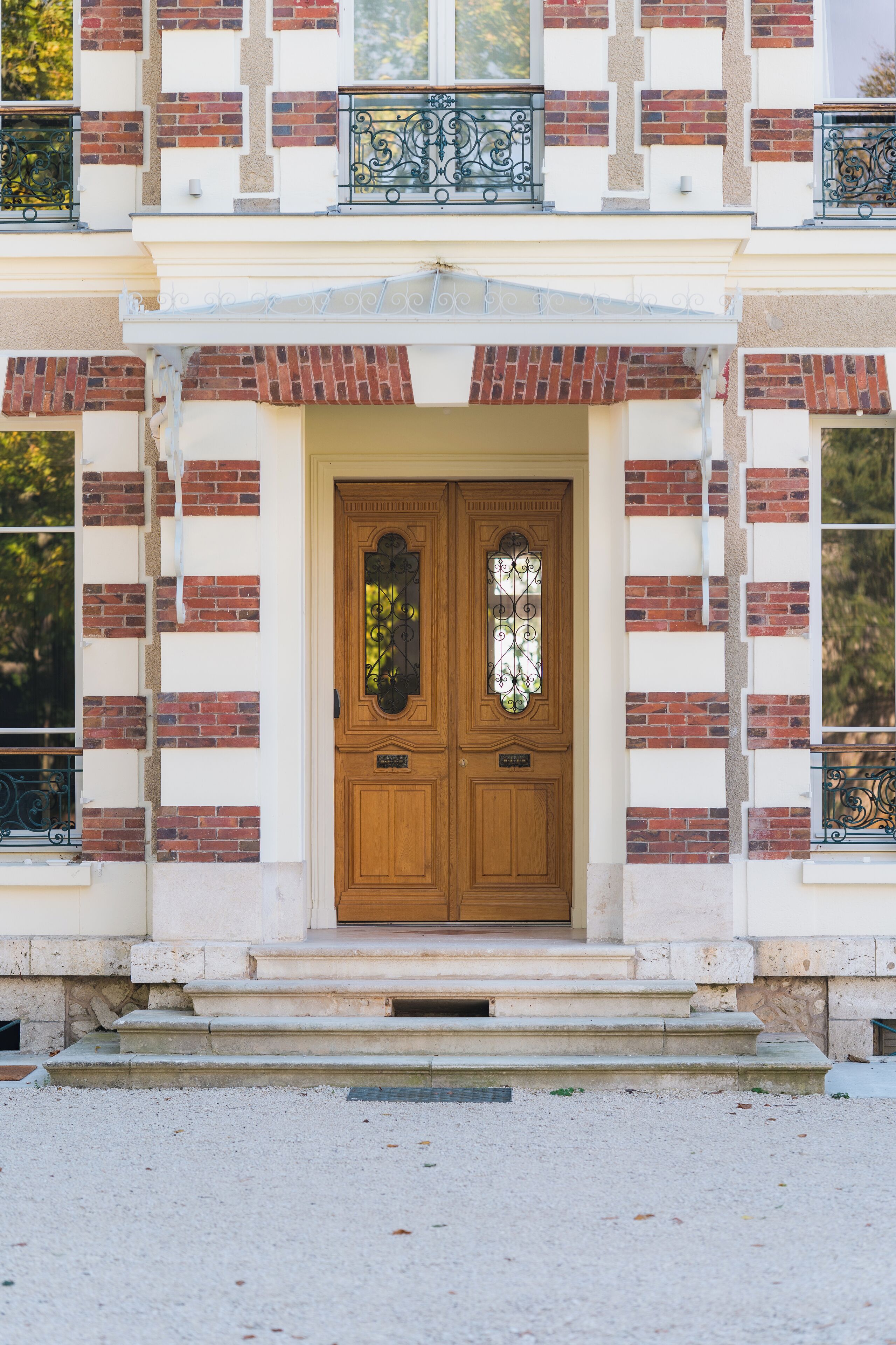 A building with a symmetrical facade, featuring a central double door with a decorative glass panel, flanked by brickwork and white stone accents.