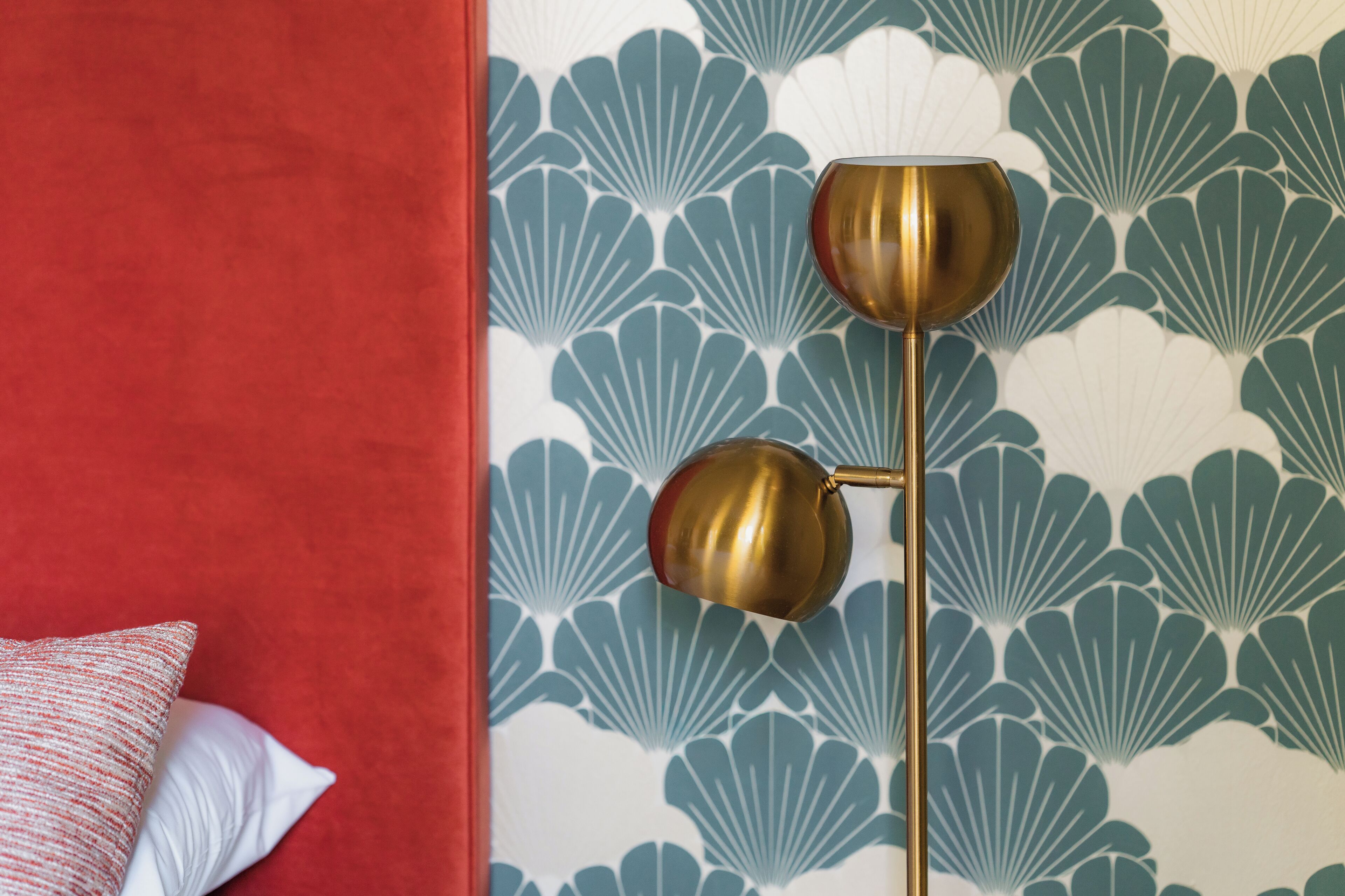 Een kamer met een rood bedovertrek, een wit kussen en een muur met een blauw-wit schelpenpatroon.
