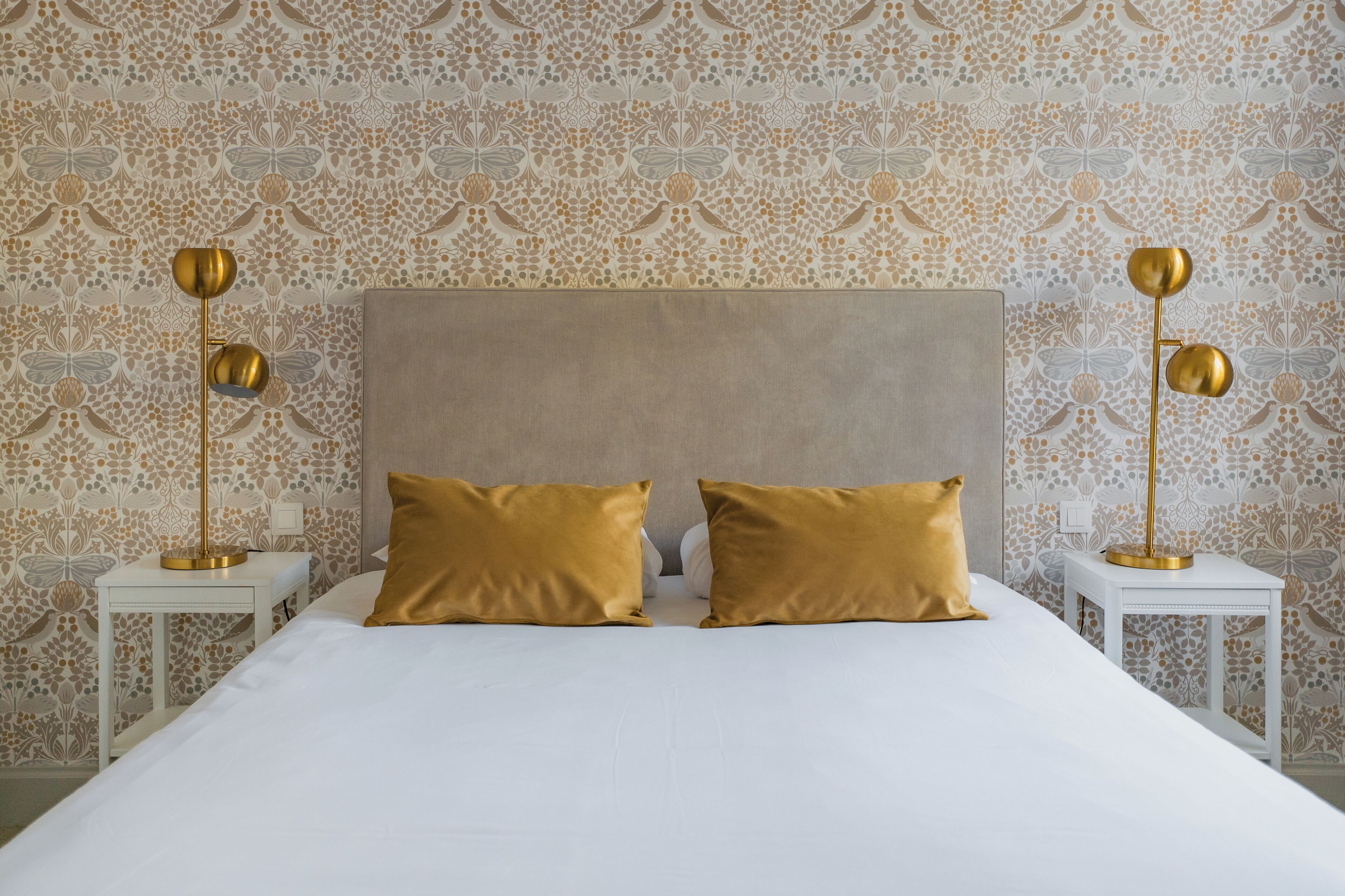 A neatly made bed with two gold pillows, a white headboard, and two bedside tables with gold lamps.