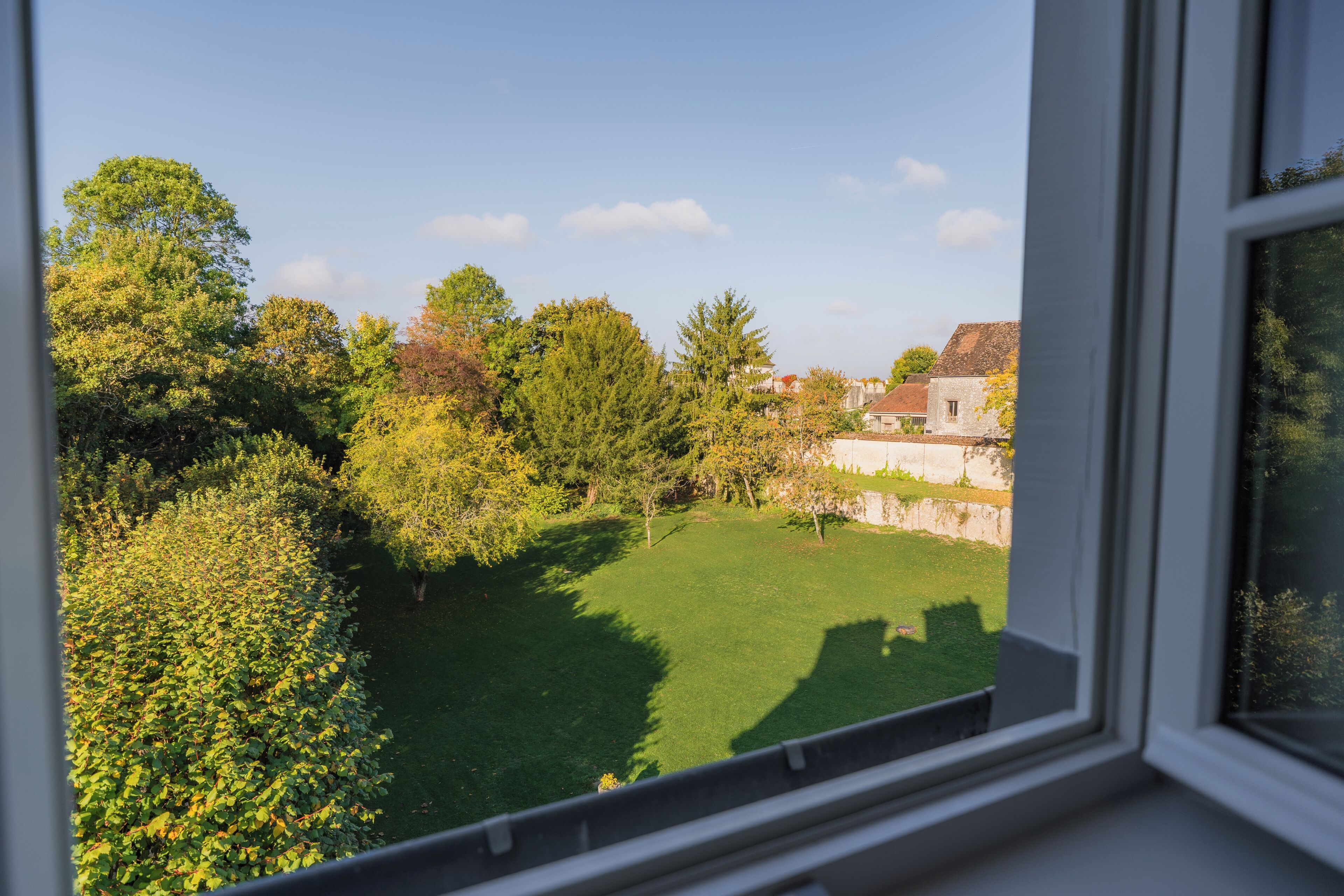 A view from a window overlooking a green lawn with trees and a stone wall.