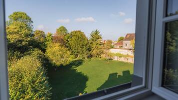 A view from a window overlooking a green lawn with trees and a stone wall.