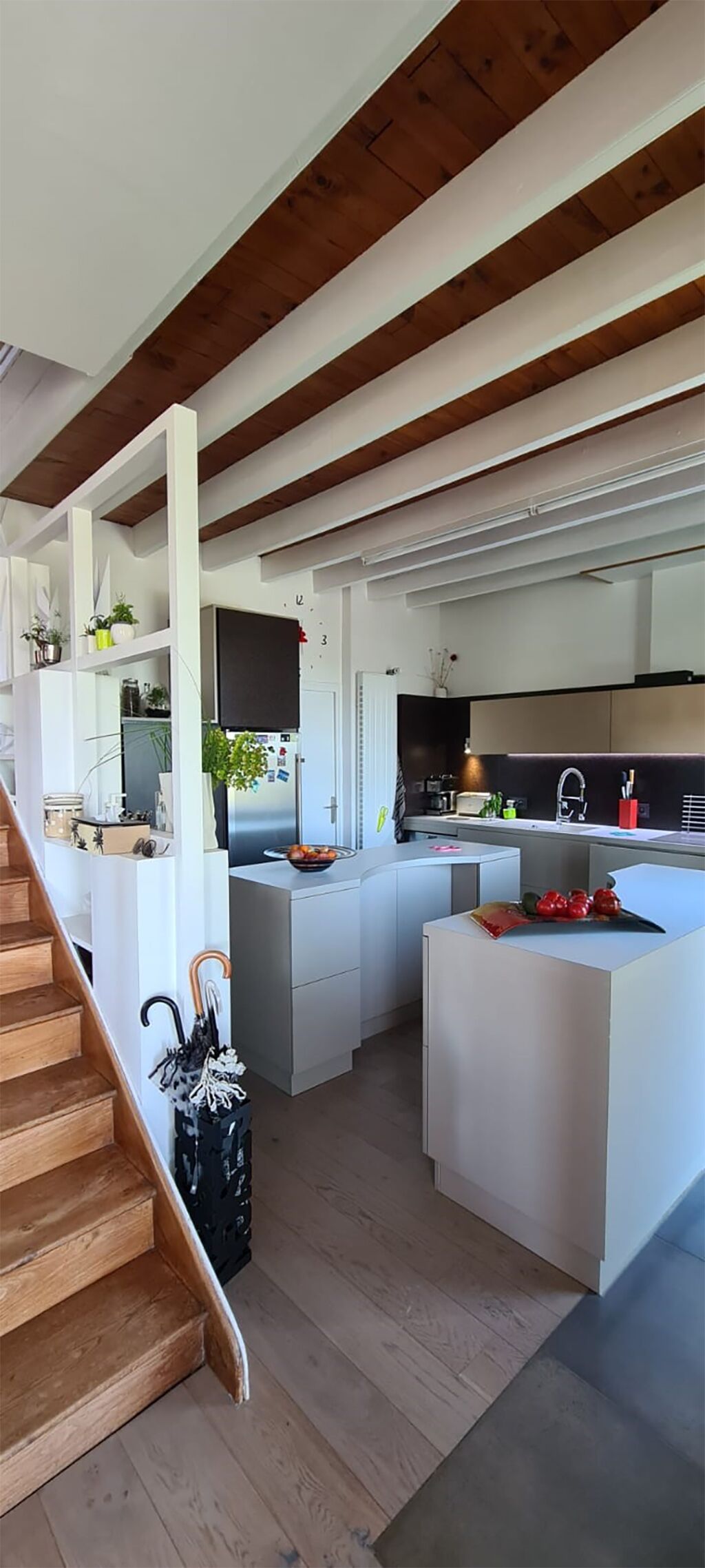 A modern kitchen with white cabinetry, a central island, and a wooden staircase.