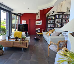 Un salon moderne avec un mur d’accent rouge, une bibliothèque, un canapé blanc et un téléviseur.