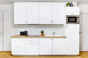 A modern kitchen with white cabinetry, a wooden countertop, a built-in microwave, and a potted plant.