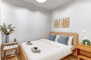 A bedroom with a bed, pillows, a nightstand, a vase with flowers, and wall art.