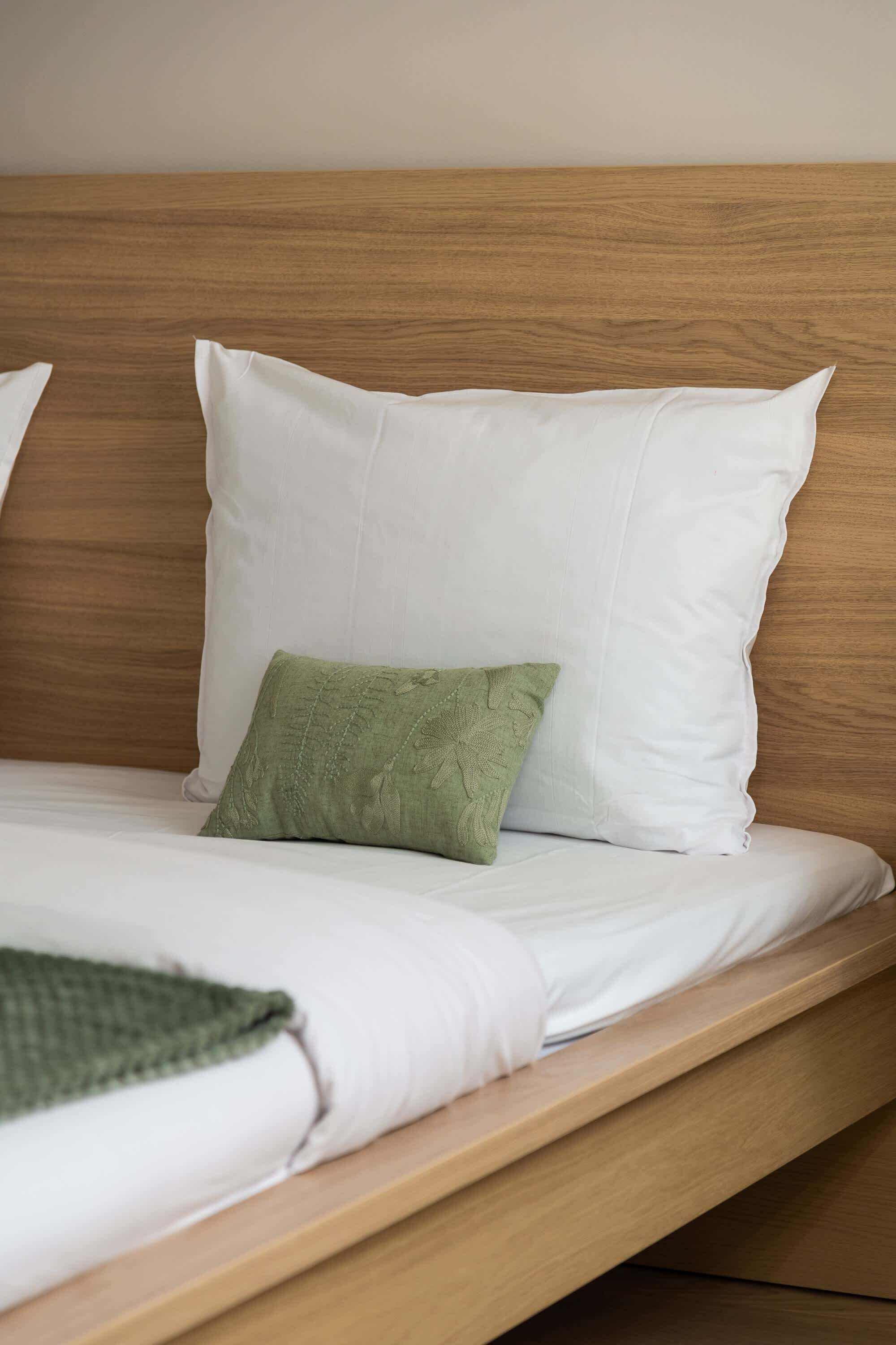 A bed with white bedding and a single green pillow.