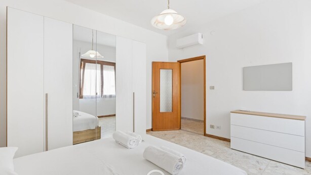 Quarto moderno com uma cama grande, um guarda-roupa, um espelho e uma mesa de cabeceira.