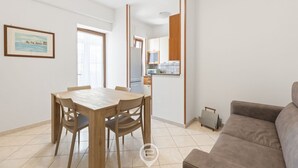 Uma sala de estar moderna com uma mesa de jantar de madeira e cadeiras, um sofá cinza e uma área de cozinha ao fundo.