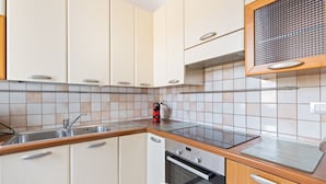 Uma cozinha moderna com armários brancos, uma pia de aço inoxidável, forno embutido e micro-ondas.
